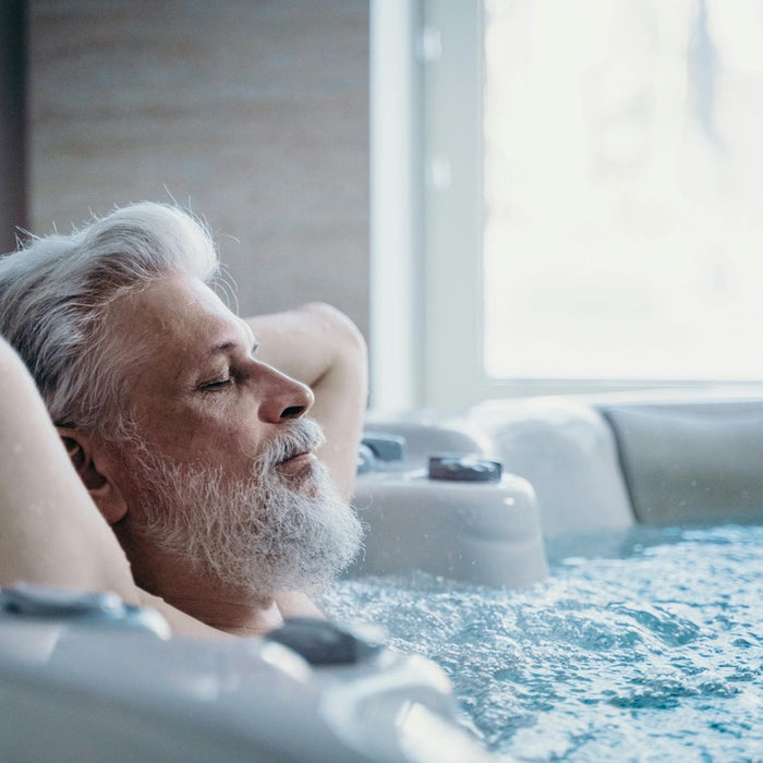 An elderly man, around 65 years old, is relaxing in a hot tub. The warm water and bubbles create a serene atmosphere, showcasing the therapeutic benefits of hot tub relaxation for seniors.